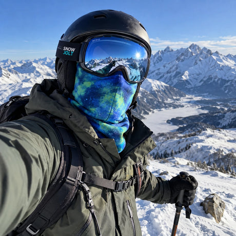 Skier taking a selfie on a snowy mountain summit wearing a blue tie-dye Snow Jolt balaclava